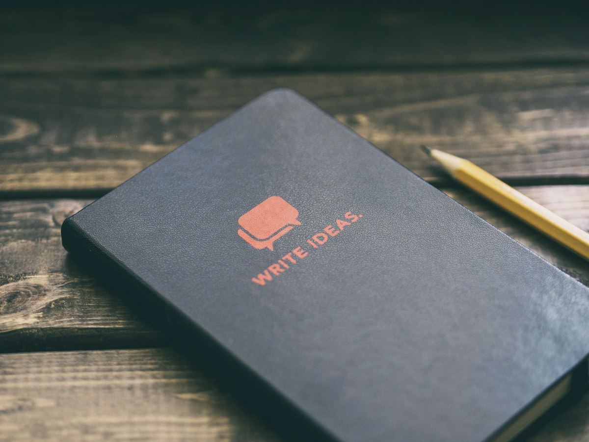 A dark notebook and a pencil on a wooden table, ready for a puzzle